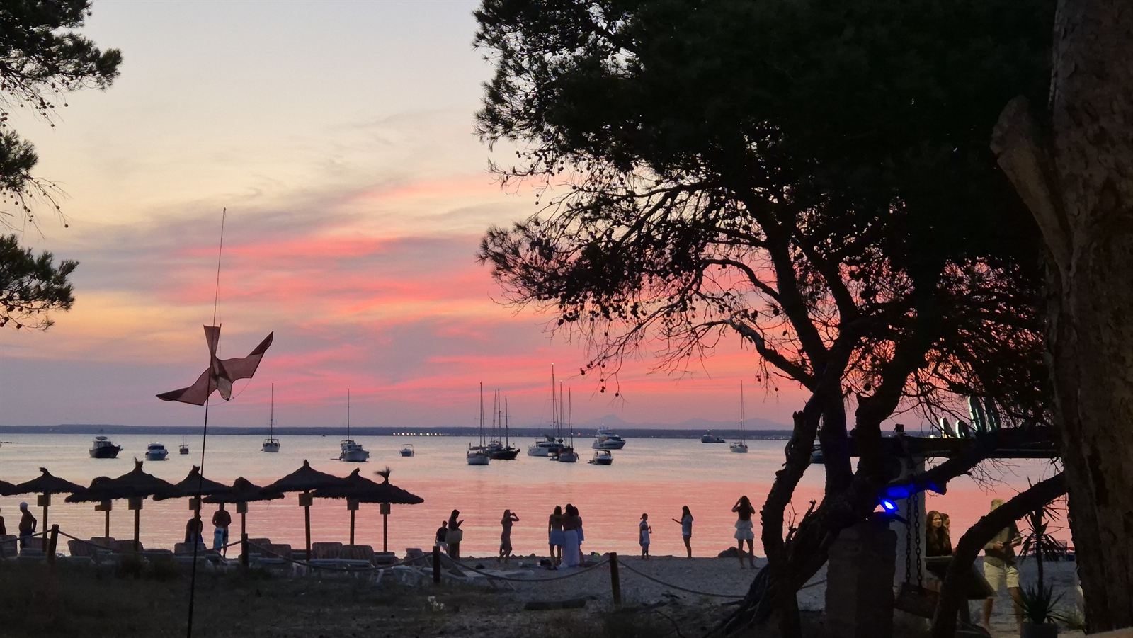 Strand mit Sonnenschirmen und Segelbooten bei rosafarbenem Sonnenuntergang