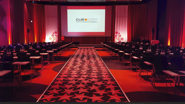 Bestuhlter Saal in rotem Licht mit Bühne und Leinwand
